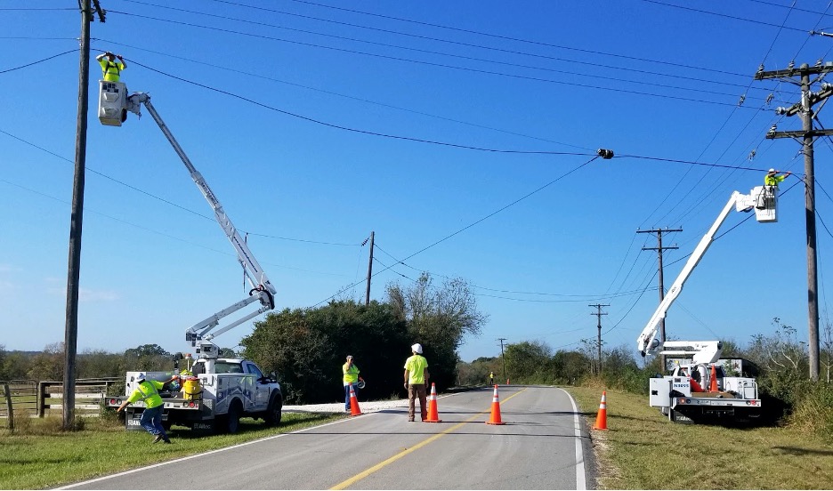 A picture showing an aerial construction team lashing fiber between two pole over a paved road.