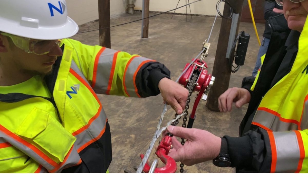 A picture showing a aerial lineman student learning how to hang steel strand cable in an indoor training facility. A picture showing a aerial lineman student learning how to hang steel strand cable in an indoor training facility.